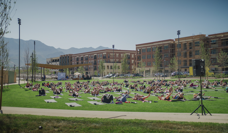 A group of 200+ people doing a strength and stretch workout outdoors on the Utah City Greenline promenade.