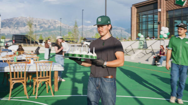 Person serving desserts on a tray at a sunny outdoor community event with mountain views at Utah City.